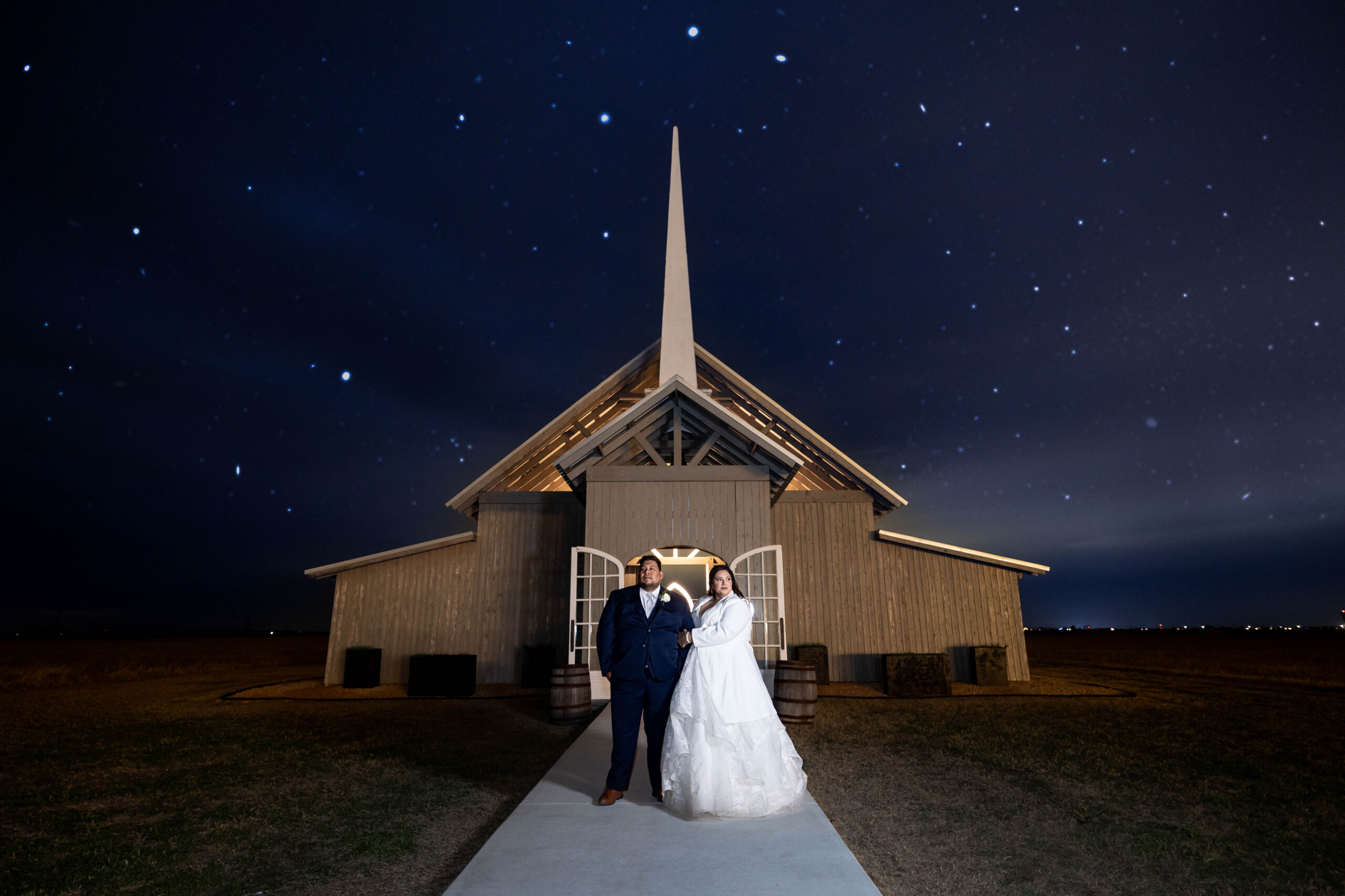 Exterior of barn reception space at The Allen Farmhaus under a starry night sky with bride and groom posed out front.